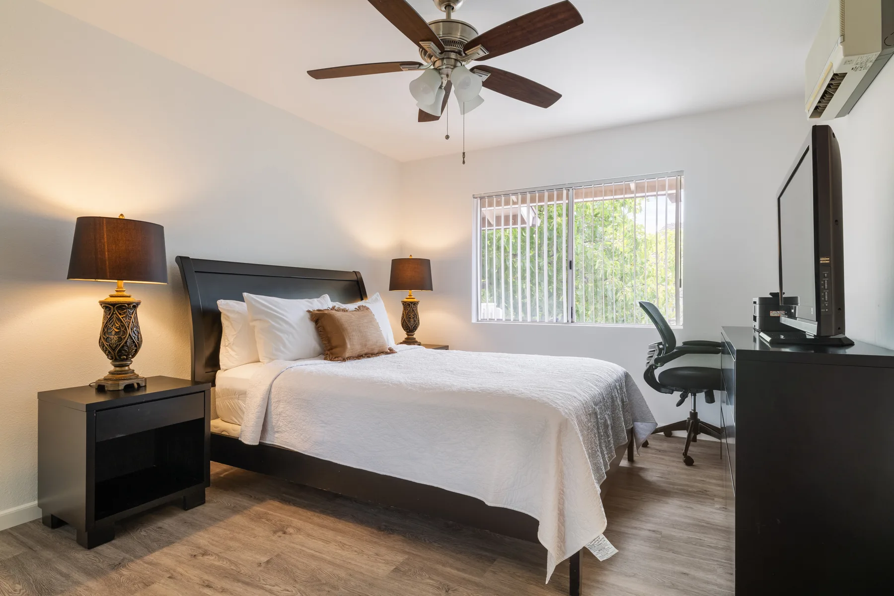 A bedroom with a neatly made bed and a window with vertical blinds.