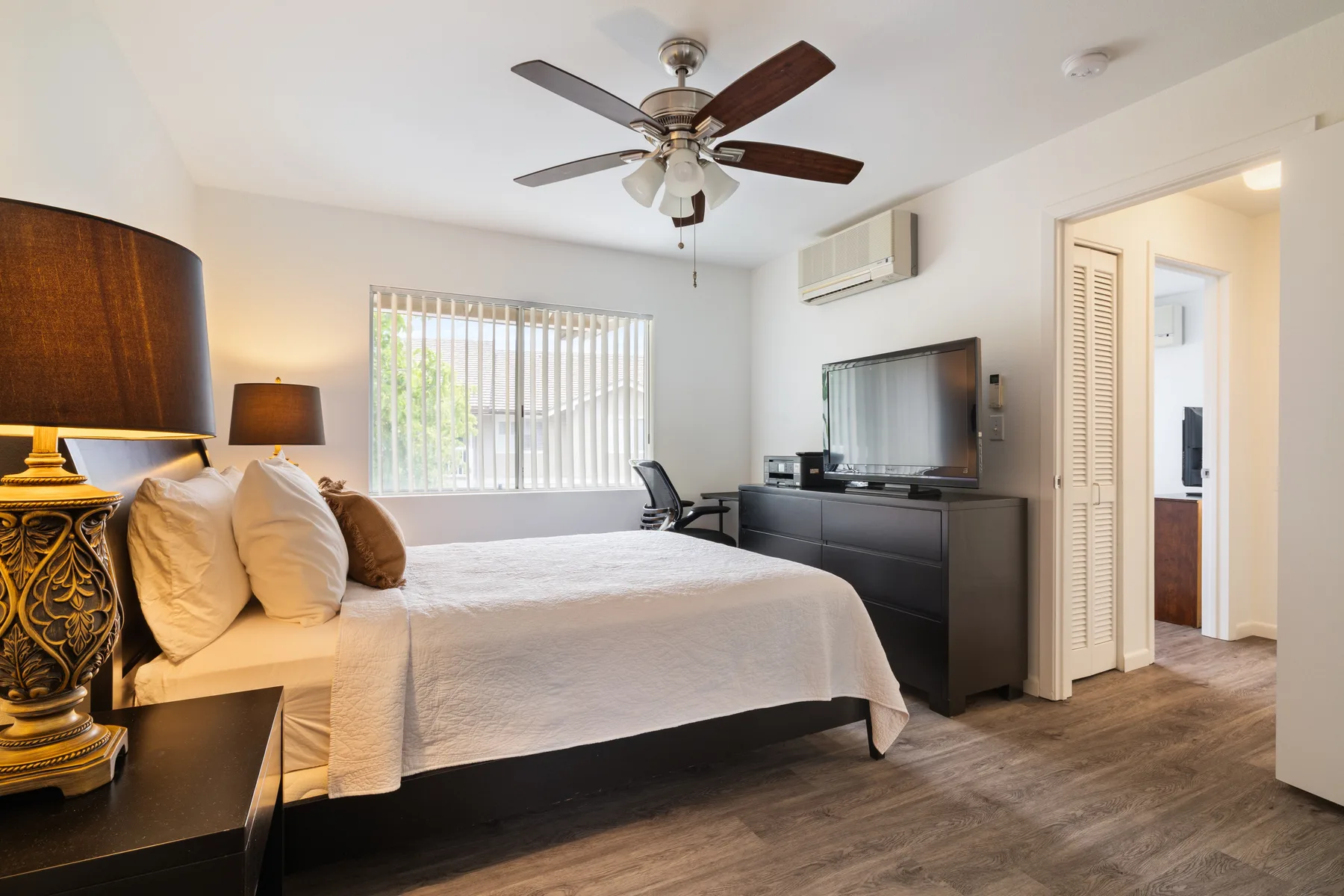A bedroom with a bed, television, and window with vertical blinds.