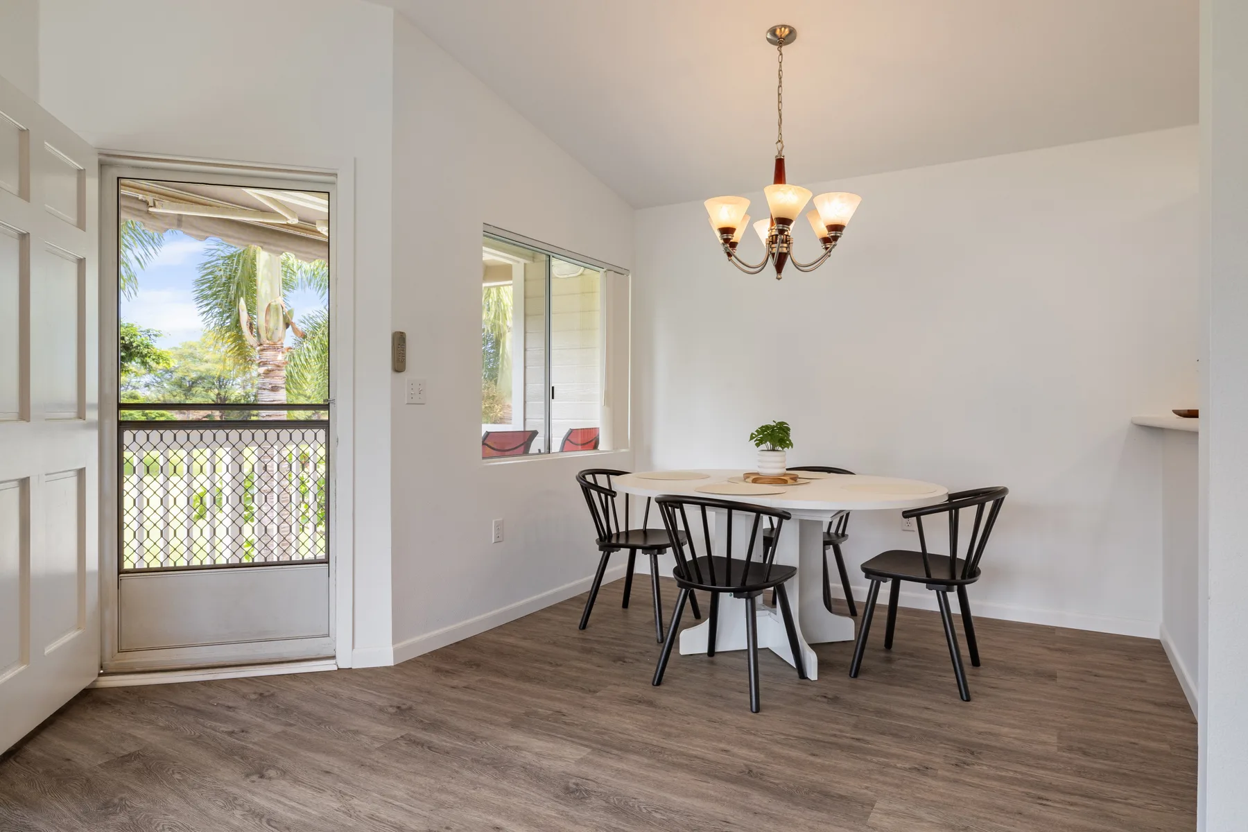 A bright dining area with a round table and chairs beneath a chandelier.
