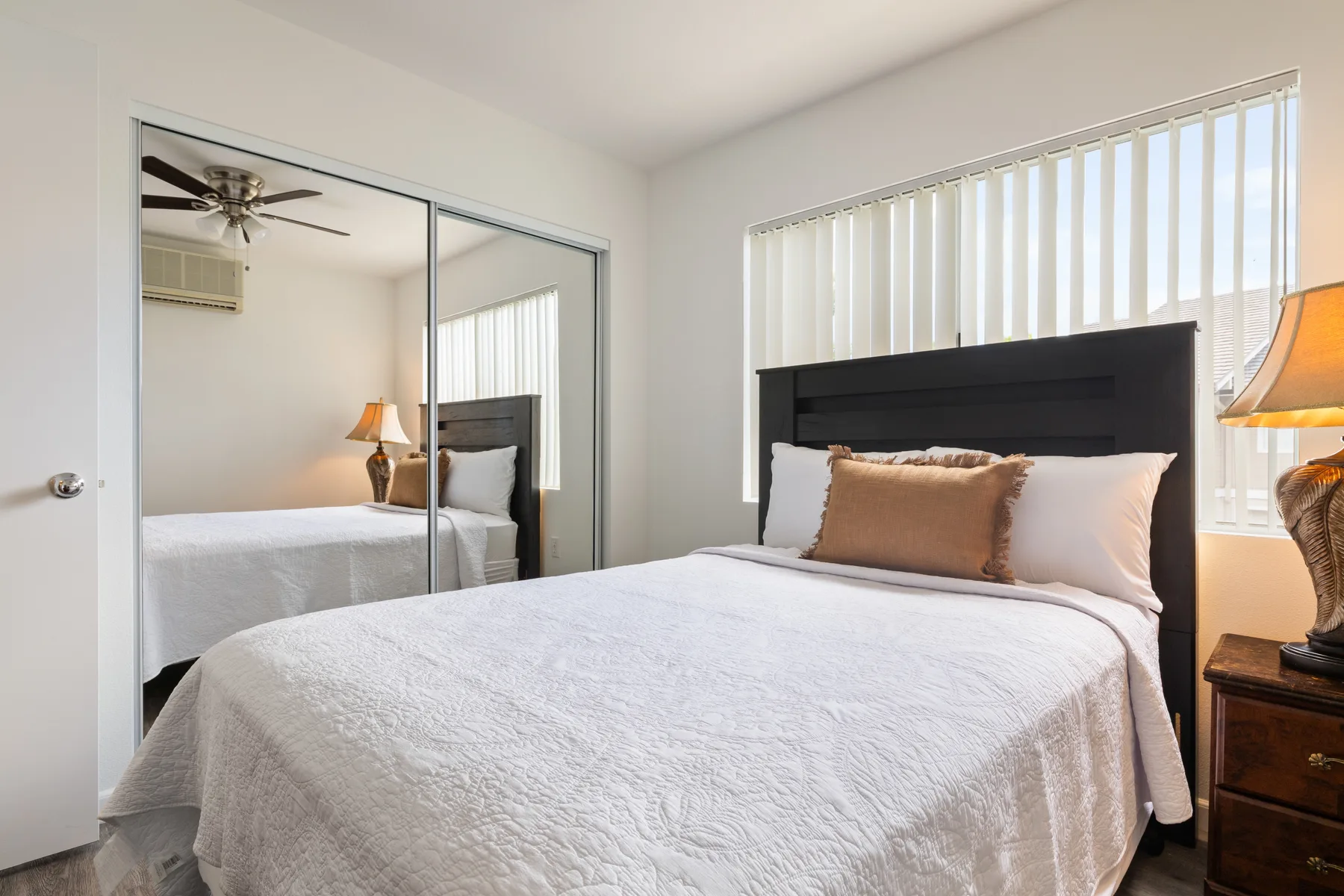 A bedroom with a neatly made bed beside a window with vertical blinds.