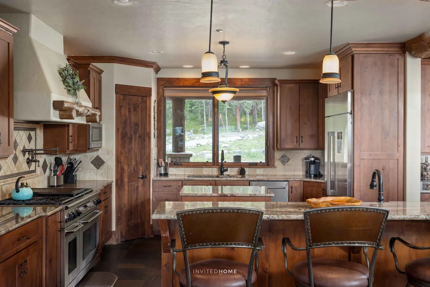 Una cocina con paneles de madera, una isla central y una ventana grande con vista a los árboles.