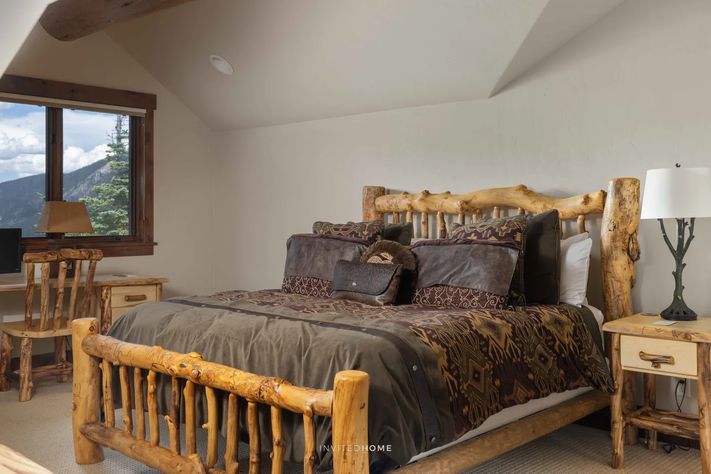 Un dormitorio con una cama de troncos, ropa de cama estampada y una ventana con vistas a las colinas.