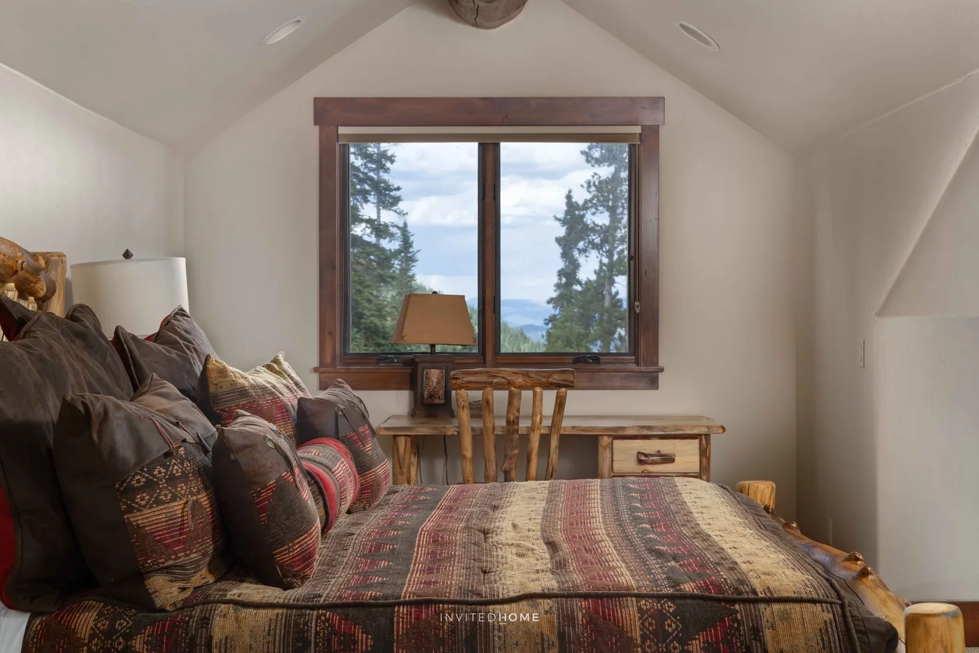 Un dormitorio con una cama estampada, un escritorio pequeño y una ventana con vista a los árboles.