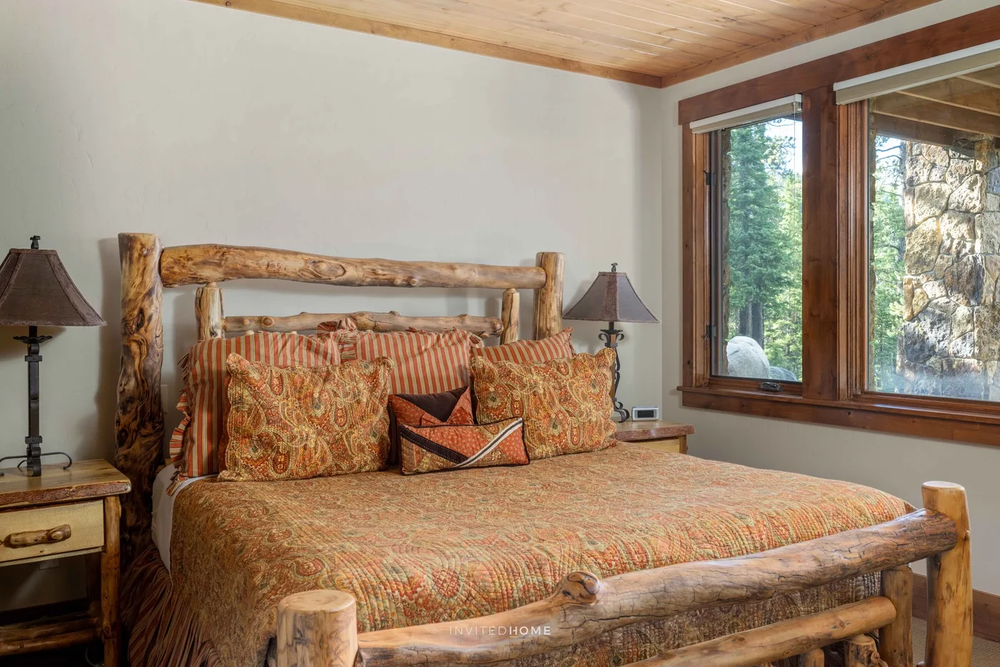 Un dormitorio con una cama de madera, ropa de cama estampada y ventanas grandes.