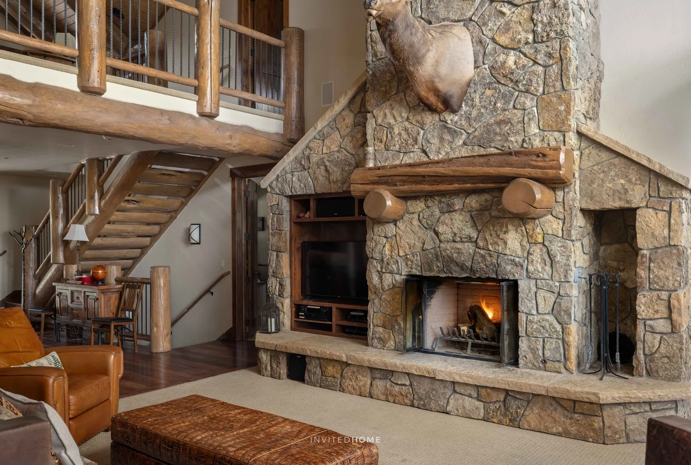 Una sala rústica se centra en una gran chimenea de piedra bajo un altillo de madera.