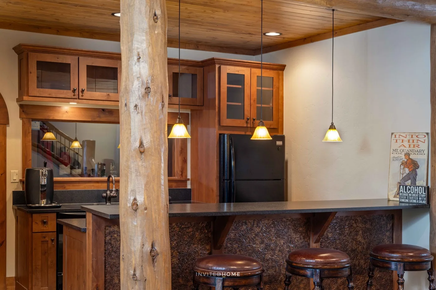 Una cocina de madera con barra, luces colgantes y taburetes.