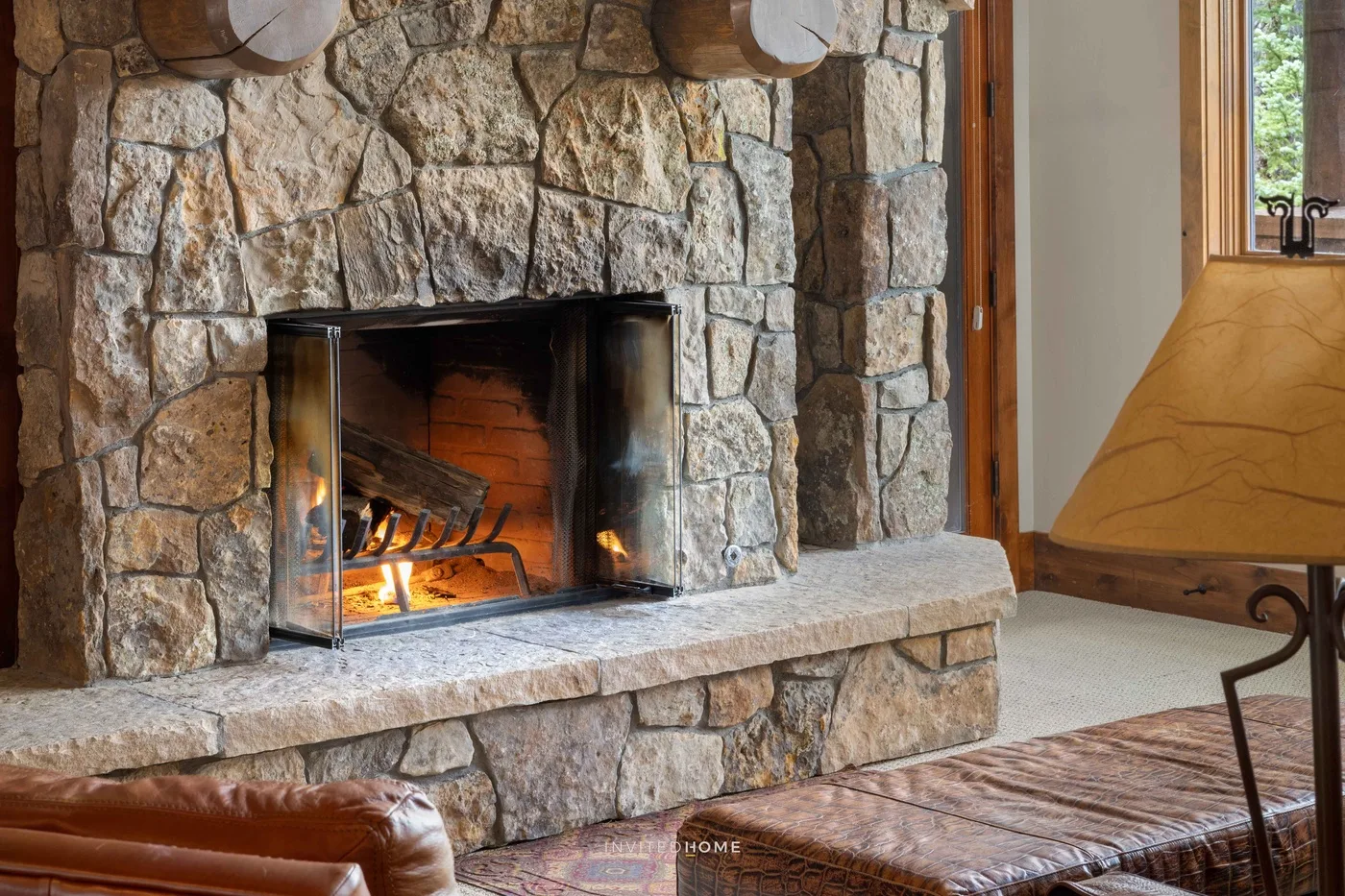 Una chimenea de piedra encendida está junto a una ventana y una zona de asientos.