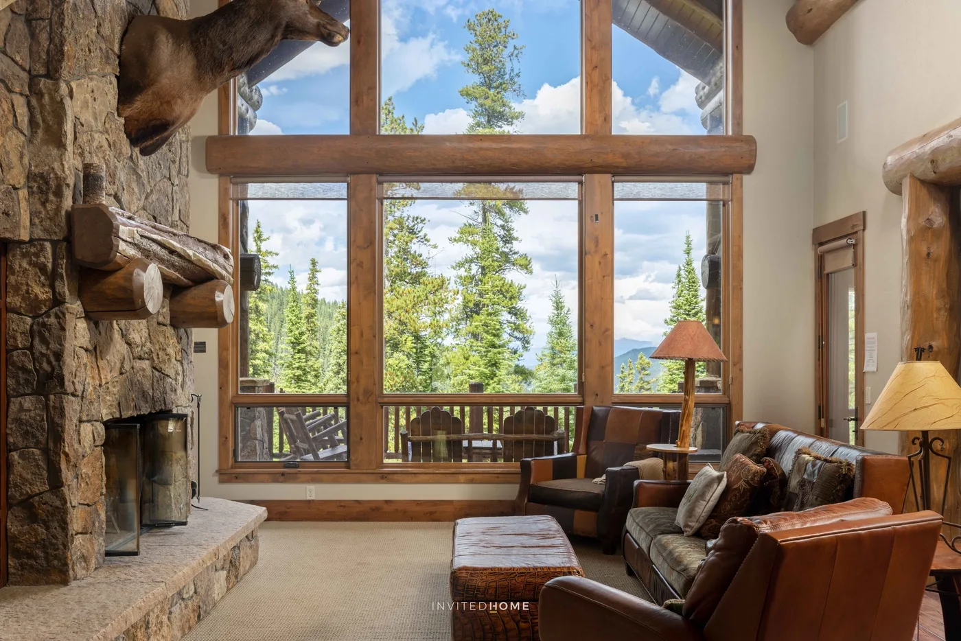 Una sala rústica con chimenea de piedra y grandes ventanas con vista a los árboles.