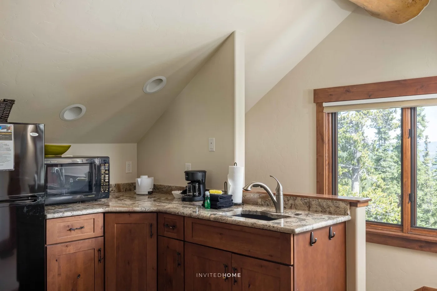 Una cocina compacta con gabinetes de madera, electrodomésticos sobre la encimera y una ventana grande.
