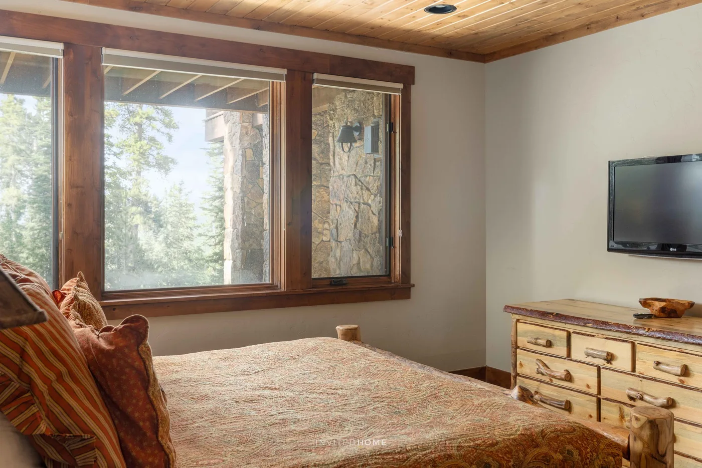 Un dormitorio con una cama grande, ventanas con molduras de madera y un televisor.