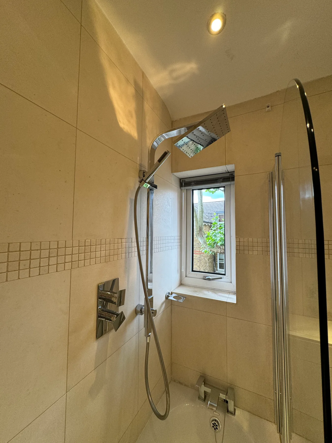 A tiled bathroom shower area with a window and handheld showerhead.