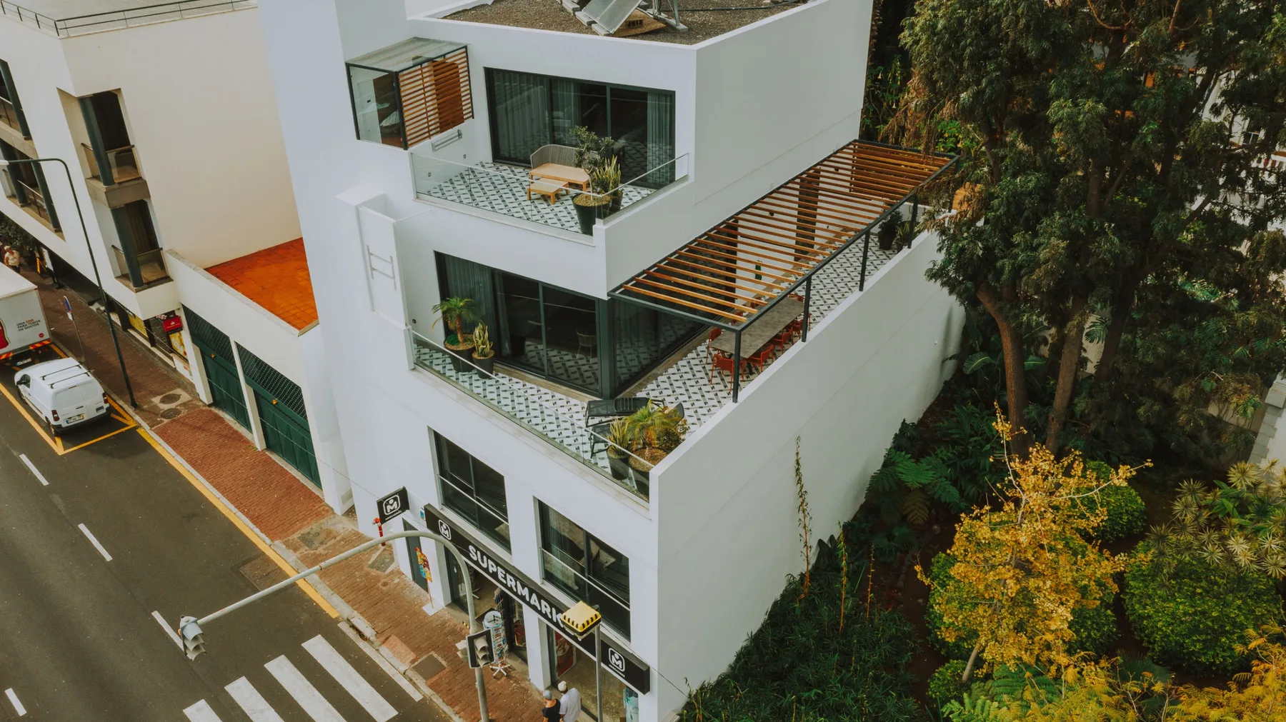 Un edificio blanco moderno con balcones se alza junto a una calle arbolada.