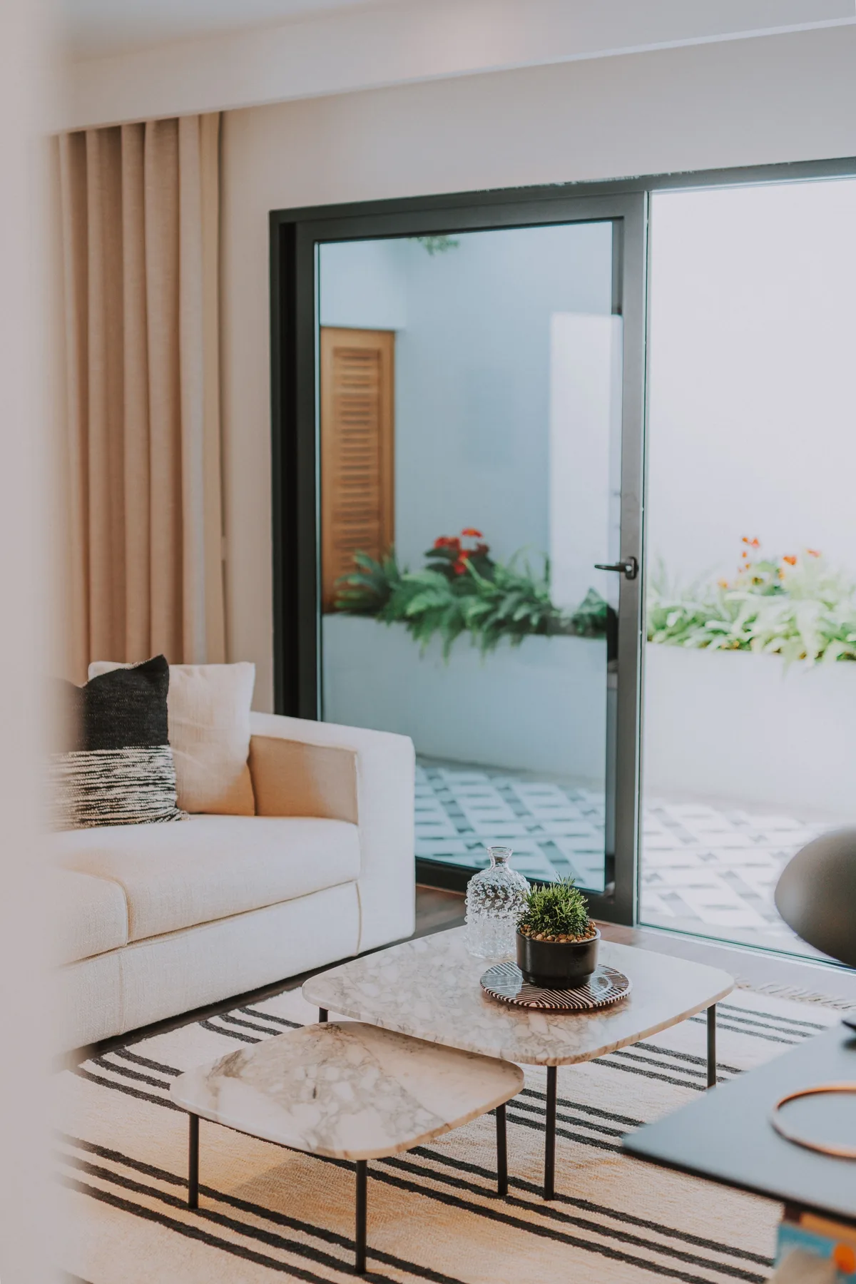 Una sala luminosa con asientos junto a una puerta de vidrio que da a un patio con plantas.