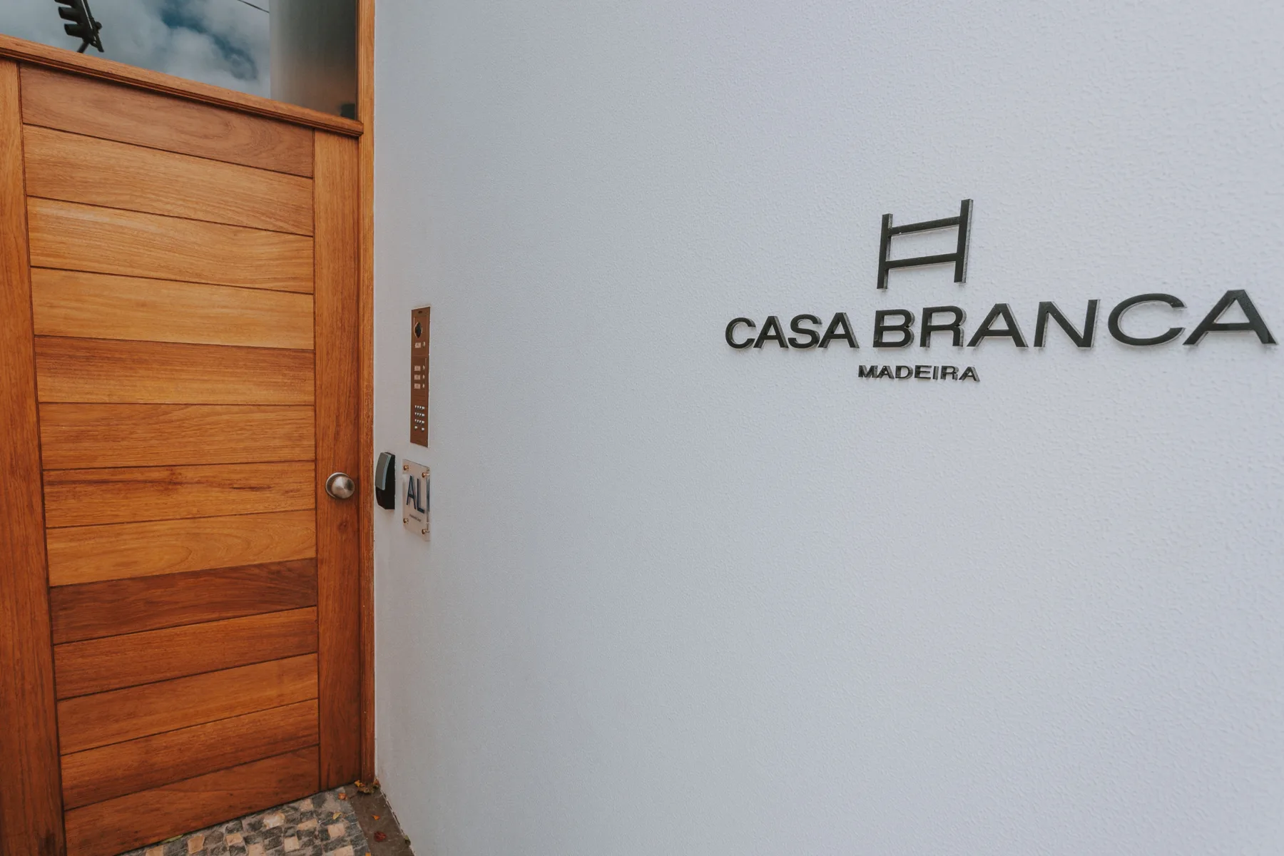 Una entrada con una puerta de madera junto a una pared blanca con un letrero.