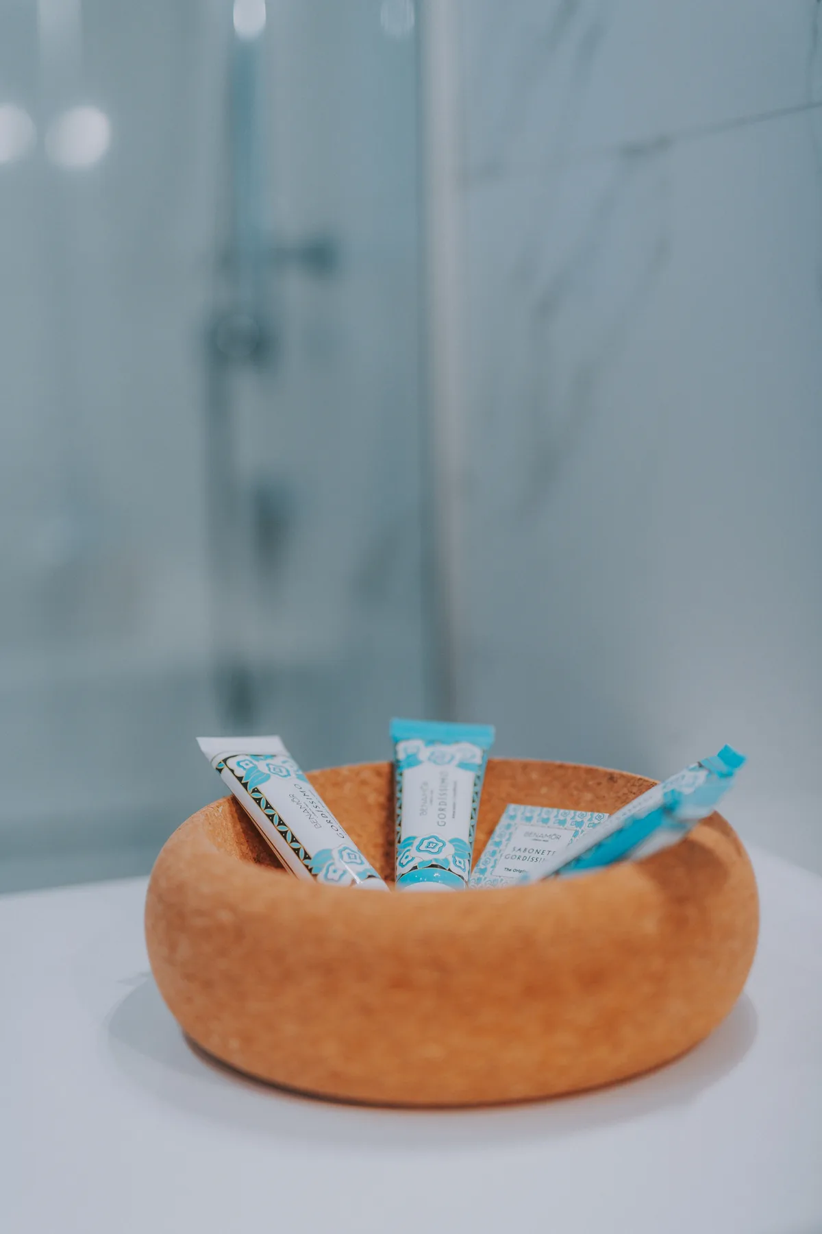 Un mostrador de baño sostiene un cuenco de madera con pequeños paquetes de artículos de aseo.