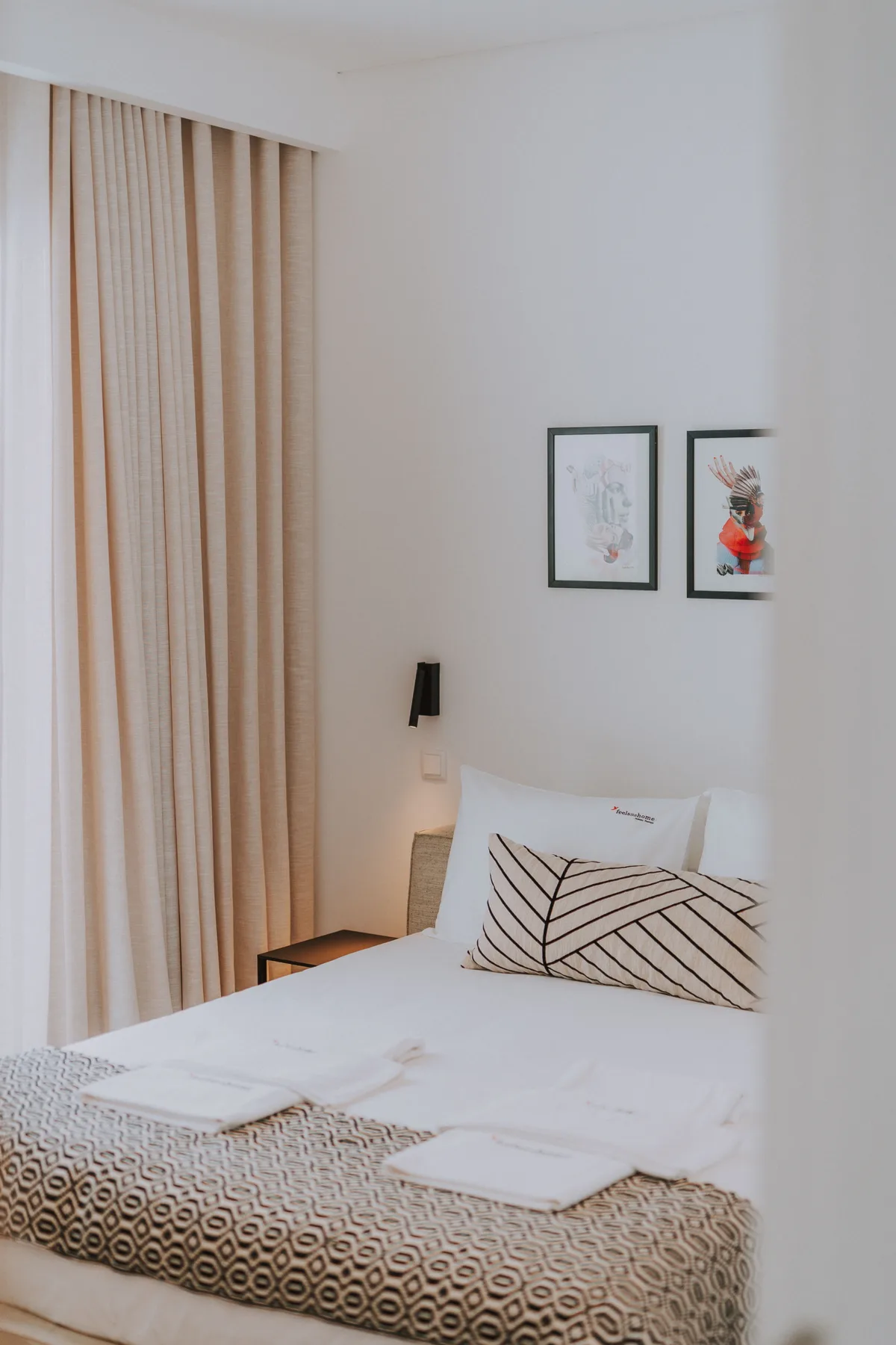 Un dormitorio luminoso con una cama bien hecha y cuadros en la pared.