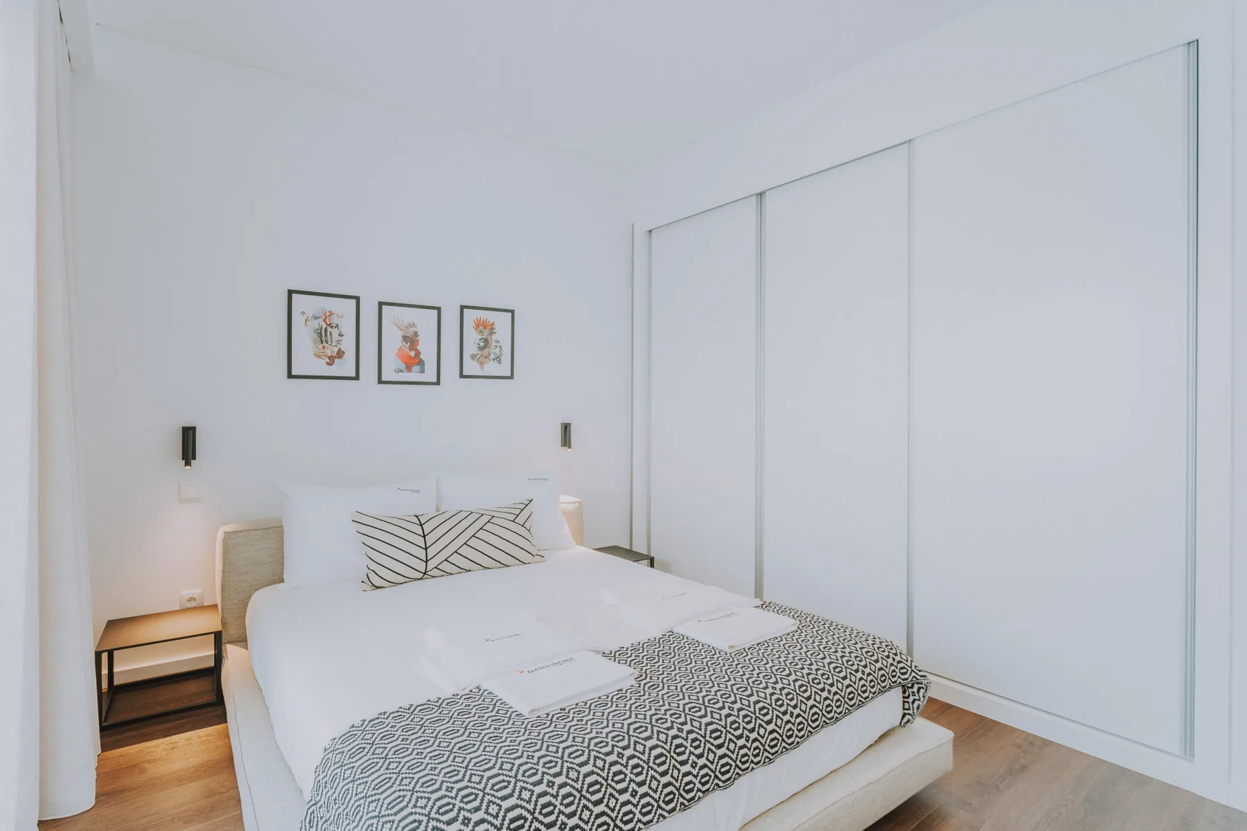 Un dormitorio luminoso con una cama bien hecha y tres cuadros en la pared.