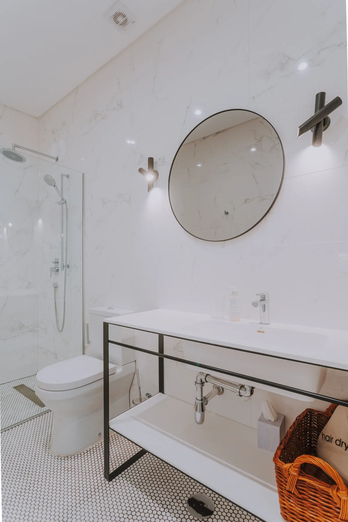 Un baño luminoso con un espejo redondo sobre el lavabo y una ducha.