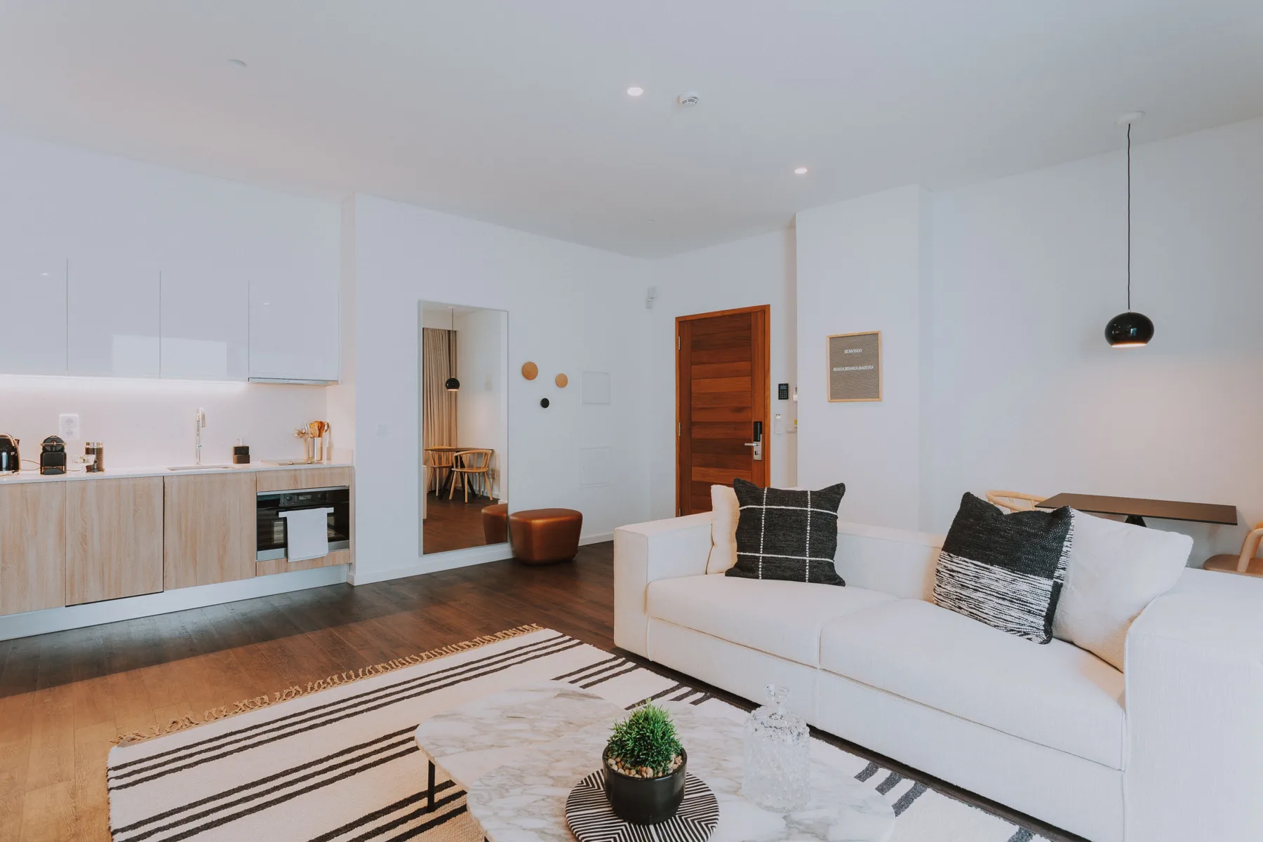 Una sala luminosa con un sofá blanco y una cocina abierta.