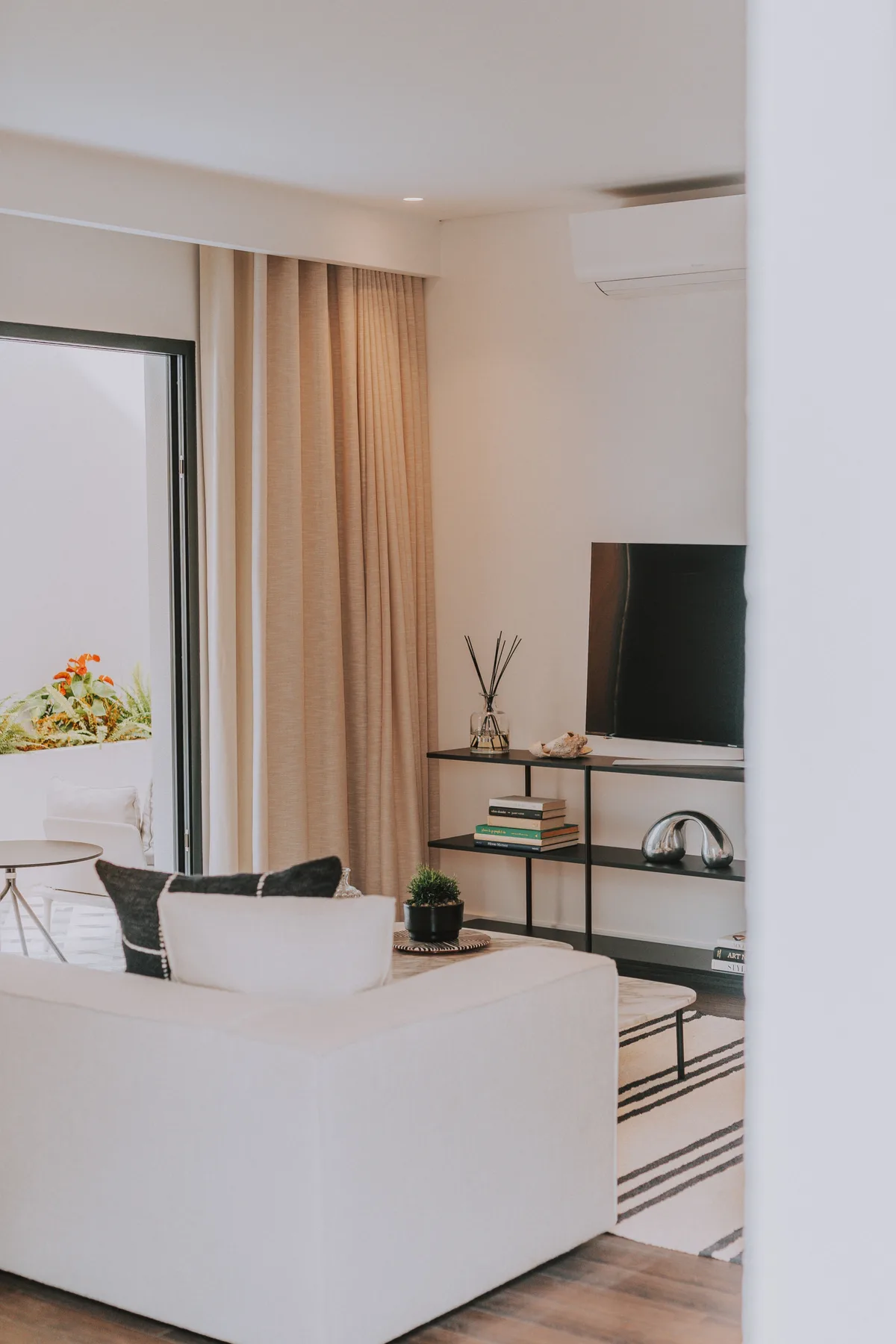 Una sala luminosa con asientos, televisor y cortinas junto a un balcón.