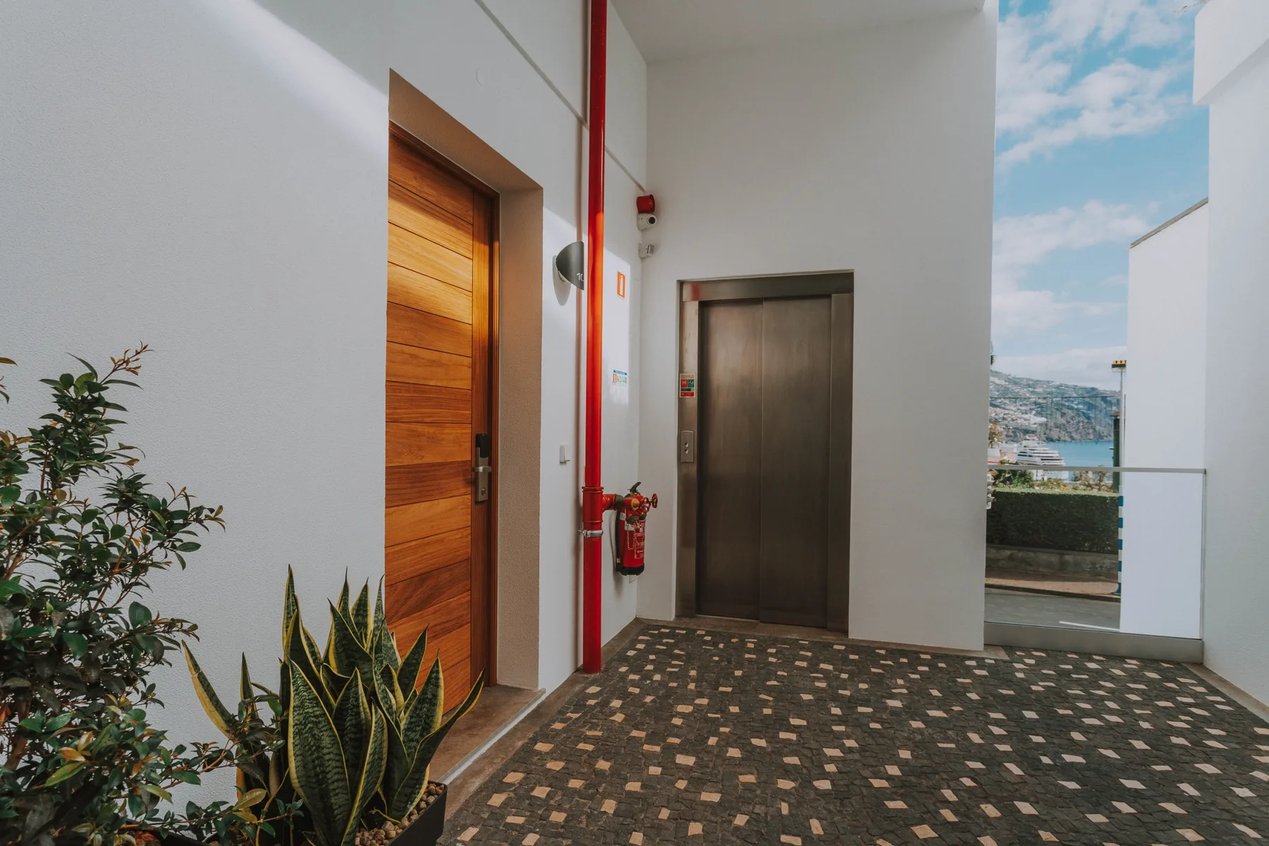 Un pasillo interior con una puerta de madera, un ascensor y vistas de la ciudad.