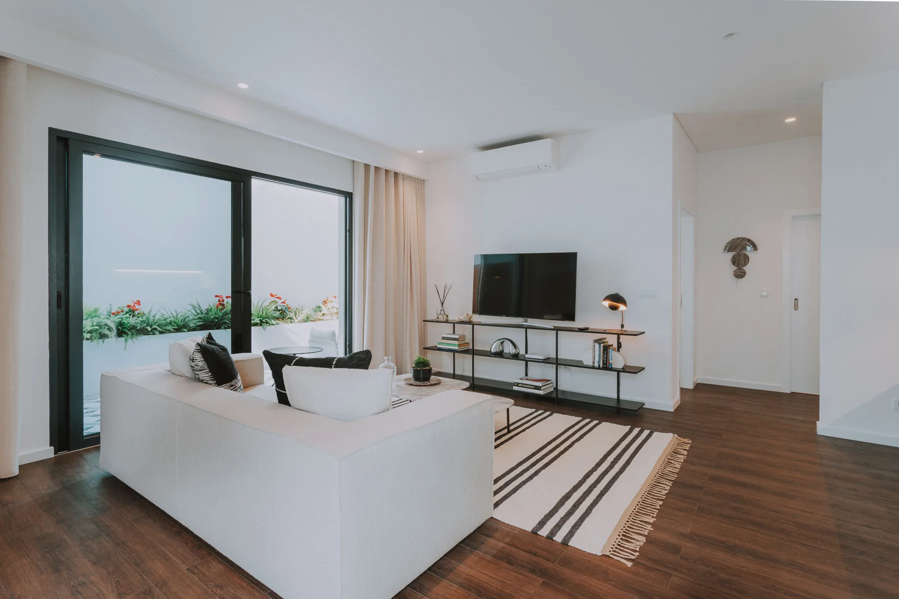 Una sala luminosa con una zona de estar, televisor y grandes ventanas.