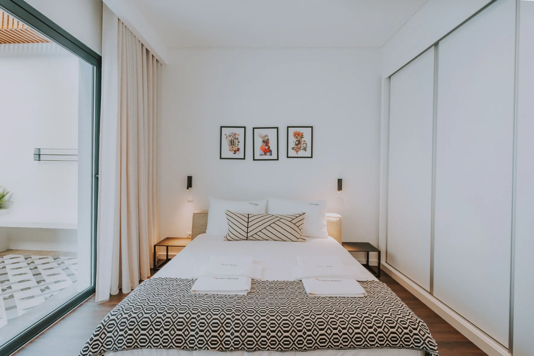 Un dormitorio con una cama bien hecha y tres cuadros enmarcados encima.