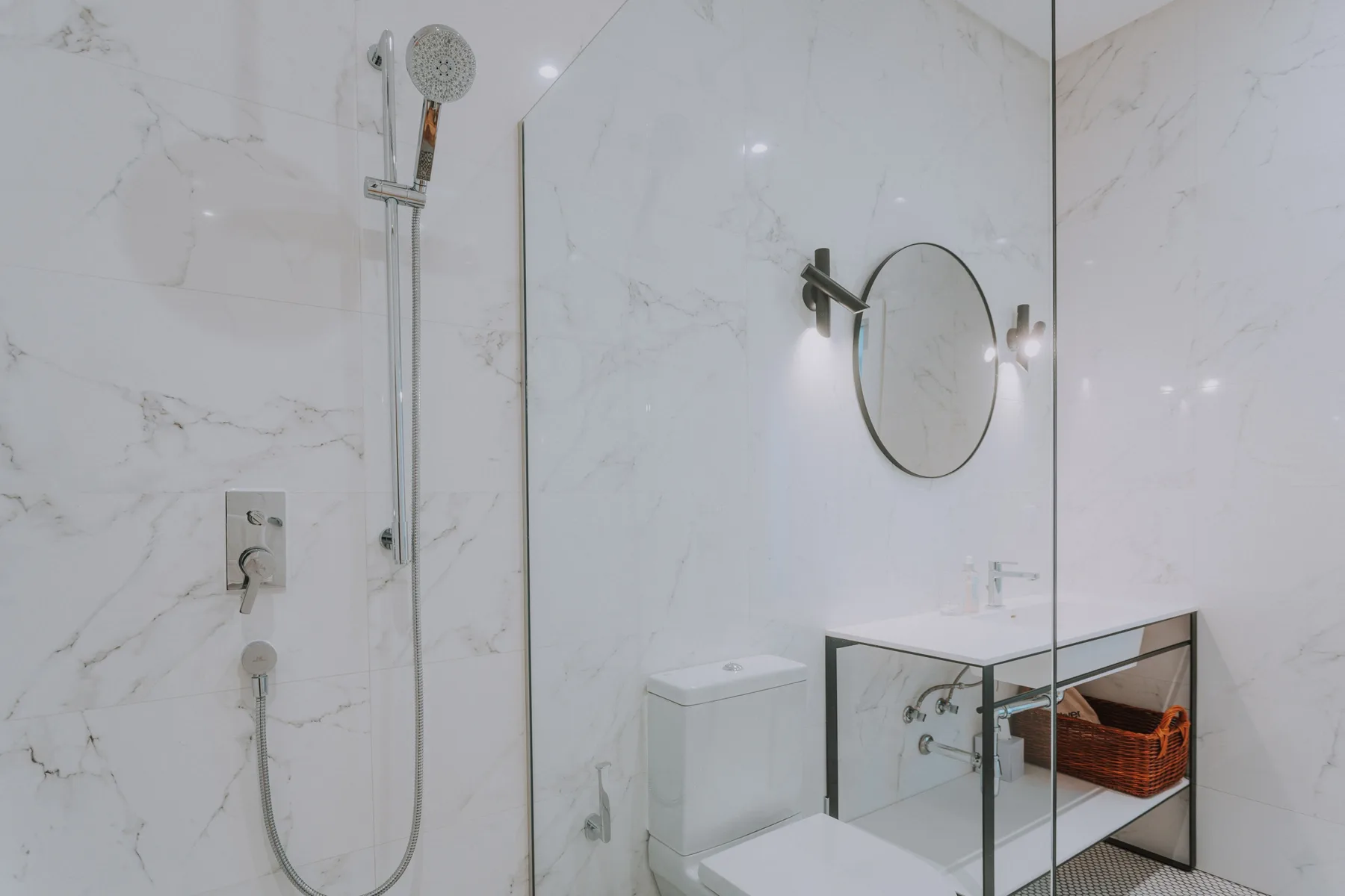 Baño luminoso con ducha de vidrio y un espejo redondo montado en la pared.