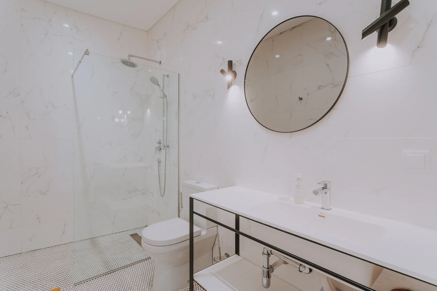 Un baño luminoso con ducha de vidrio, inodoro y un lavabo largo.