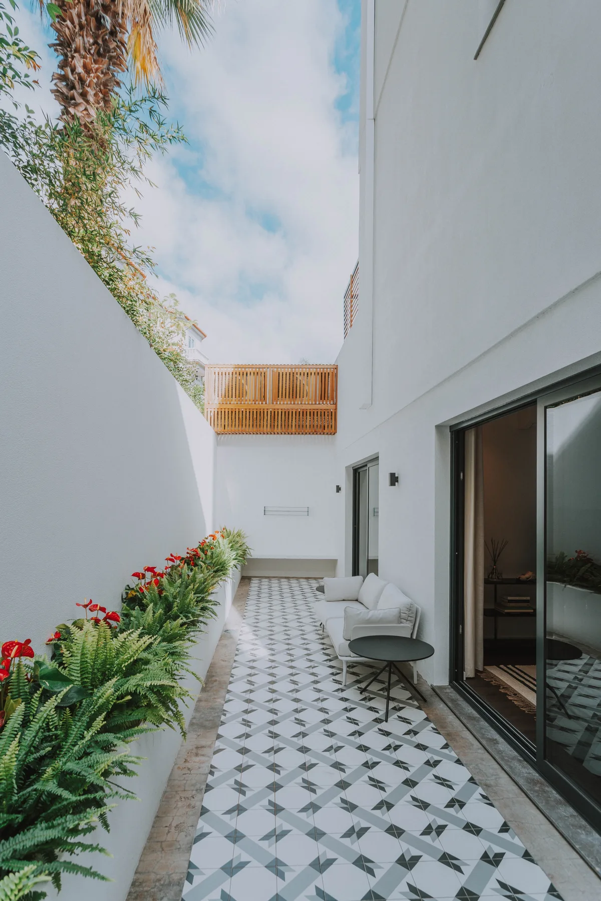 Patio exterior con suelo de baldosas y plantas junto a un edificio blanco.