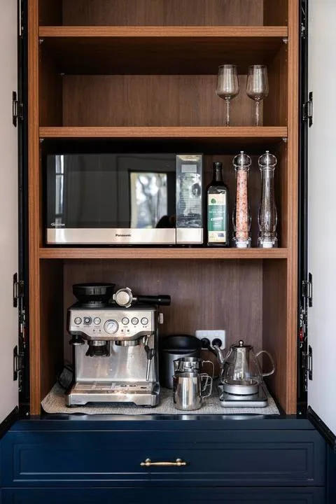 Un rincón de café empotrado con una cafetera espresso, un microondas y cristalería.