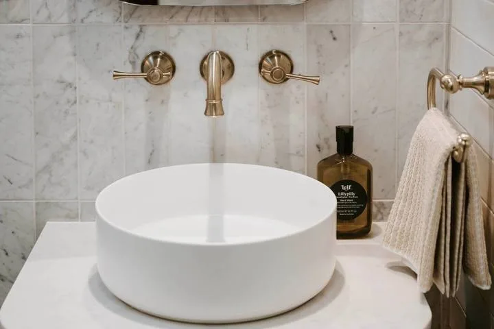 Un tocador de baño con lavabo de recipiente blanco y grifo de pared.