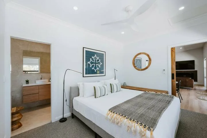 Un dormitorio luminoso con una cama bien tendida y cuadros en la pared.
