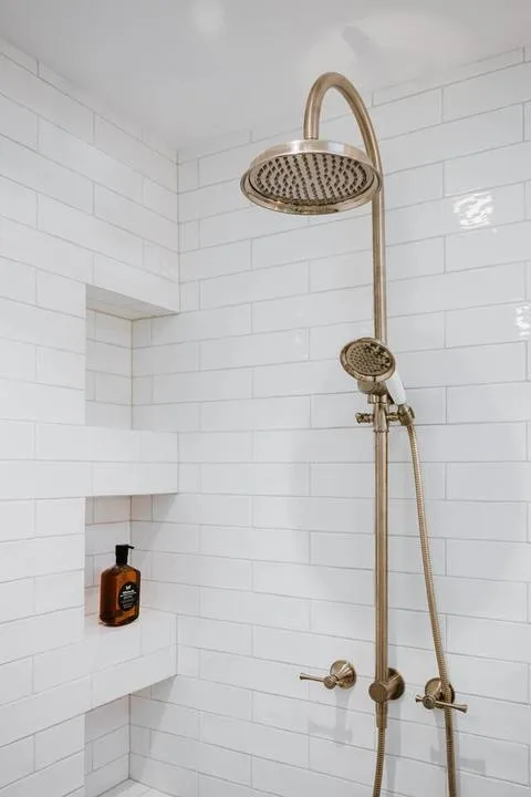 Una ducha alicatada con un cabezal y una ducha de mano de color dorado.