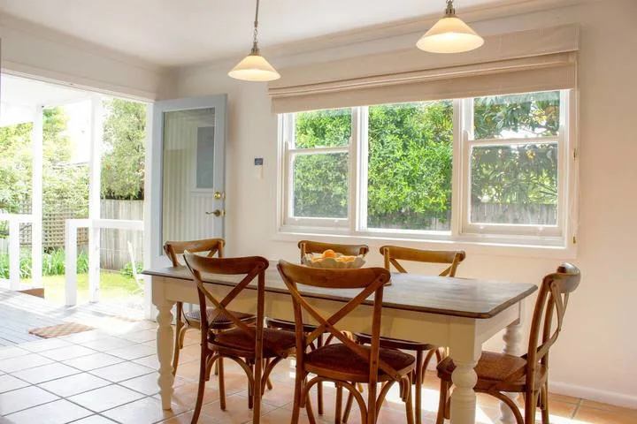 Un comedor luminoso con una mesa de madera y sillas junto a grandes ventanas.