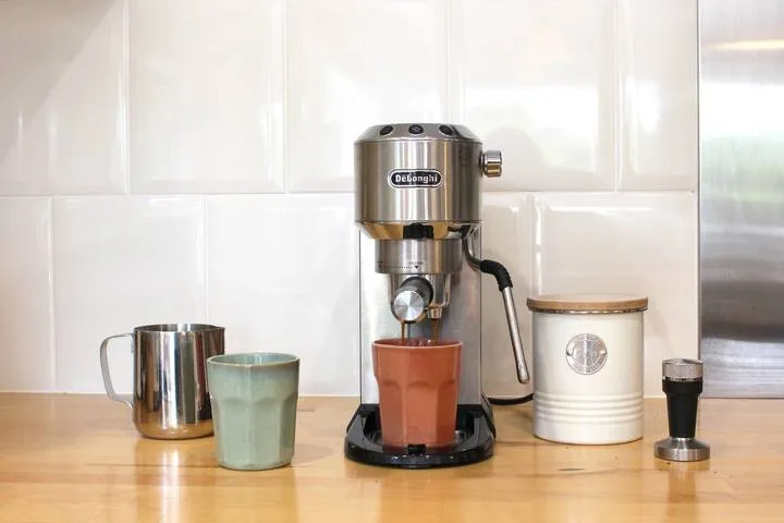 Un equipo para preparar café está sobre una encimera de madera frente a una pared de azulejos blancos.