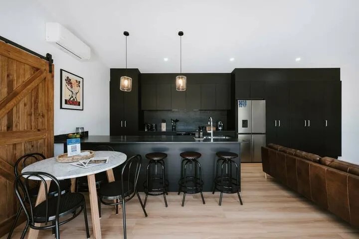 Una cocina abierta y zona de comedor con gabinetes oscuros y una mesa pequeña.