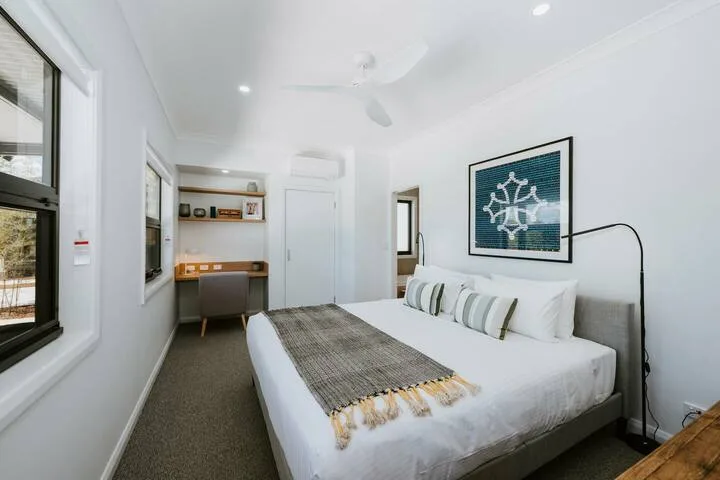 Un dormitorio luminoso con una cama, almohadas a rayas y un cuadro en la pared.