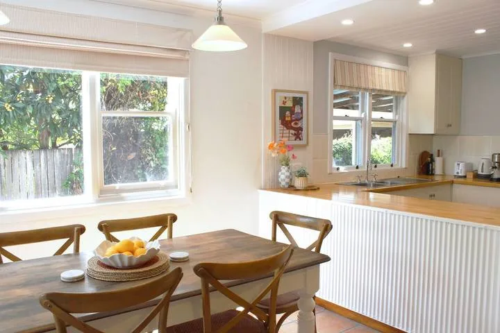 Una cocina luminosa con comedor y una mesa de madera junto a grandes ventanas.