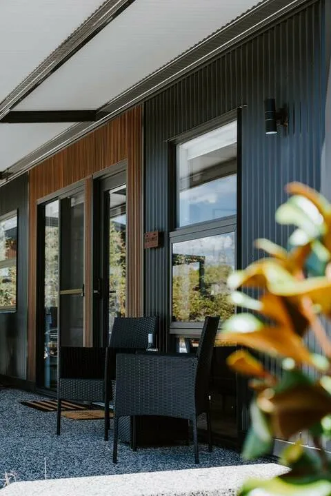 Un patio al aire libre con asientos tejidos oscuros junto a grandes ventanas.