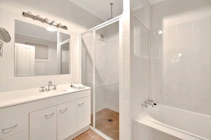 Un baño luminoso con un mueble de lavabo largo, espejo y ducha de vidrio.