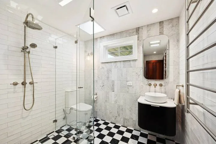 Un baño con ducha de cristal, lavabo y suelo de baldosas blancas y negras.