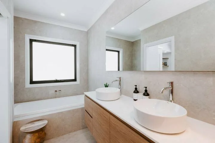 Un baño luminoso con un tocador largo, dos lavabos sobre encimera y una bañera.