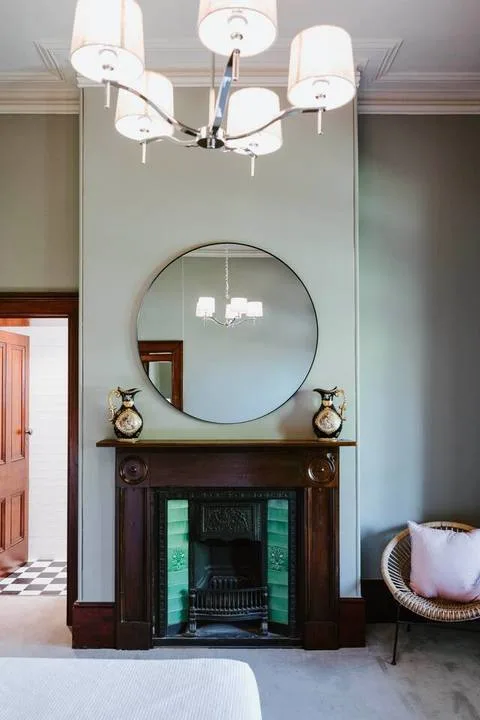 Una chimenea en la sala de estar queda bajo un gran espejo redondo, con una silla al lado.