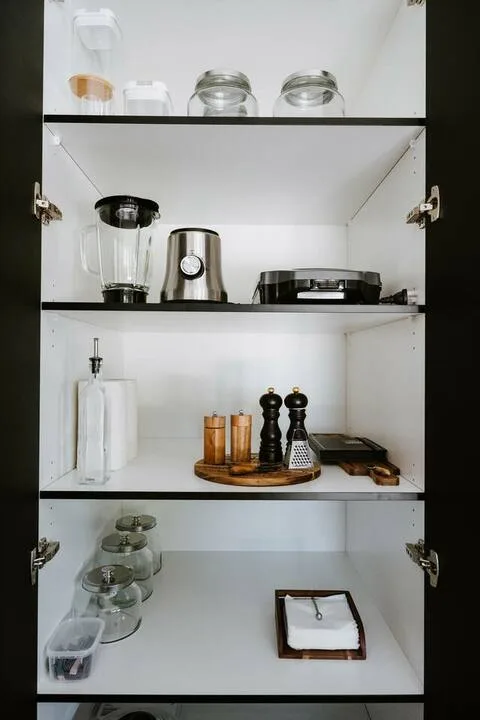 Un armario de cocina abierto muestra pequeños electrodomésticos, frascos y utensilios de cocina.