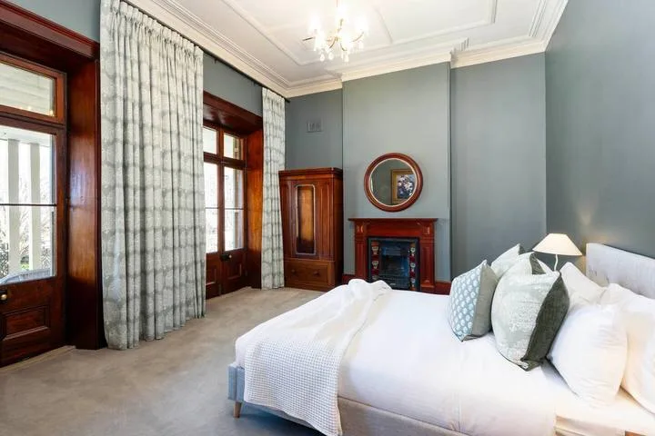 Un dormitorio con una cama grande, ventanas altas y una chimenea.