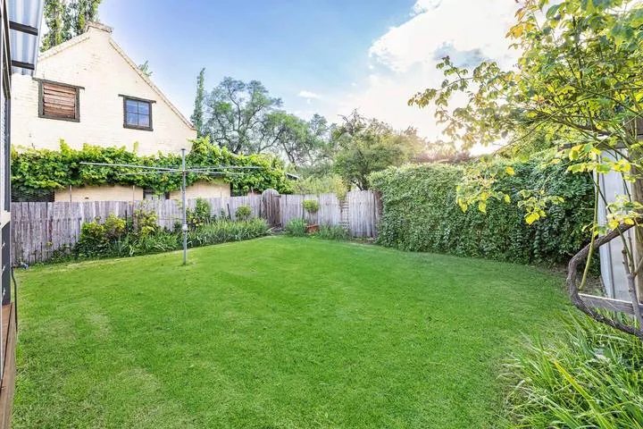 Un jardín con un amplio césped verde, setos frondosos y una cerca de madera.