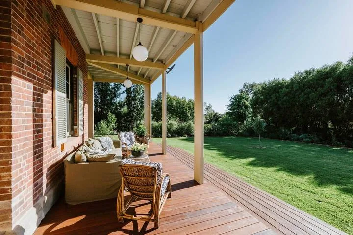 Una terraza de madera cubierta junto a una casa de ladrillo da a un césped verde.