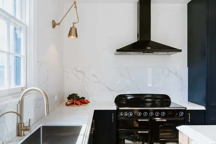 Una cocina con una estufa negra bajo una campana extractora oscura.