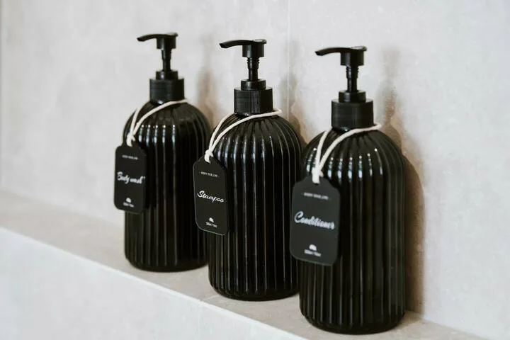 Tres botellas oscuras con dispensador están sobre un borde blanco del baño.